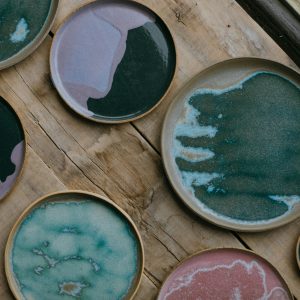 Collection of handcrafted ceramic plates featuring unique glaze patterns on wooden surface.