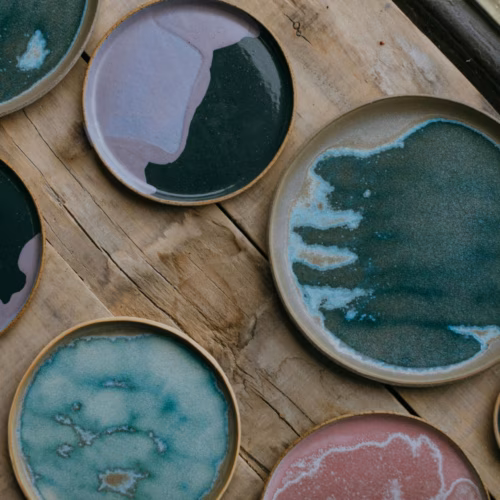 Collection of handcrafted ceramic plates featuring unique glaze patterns on wooden surface.