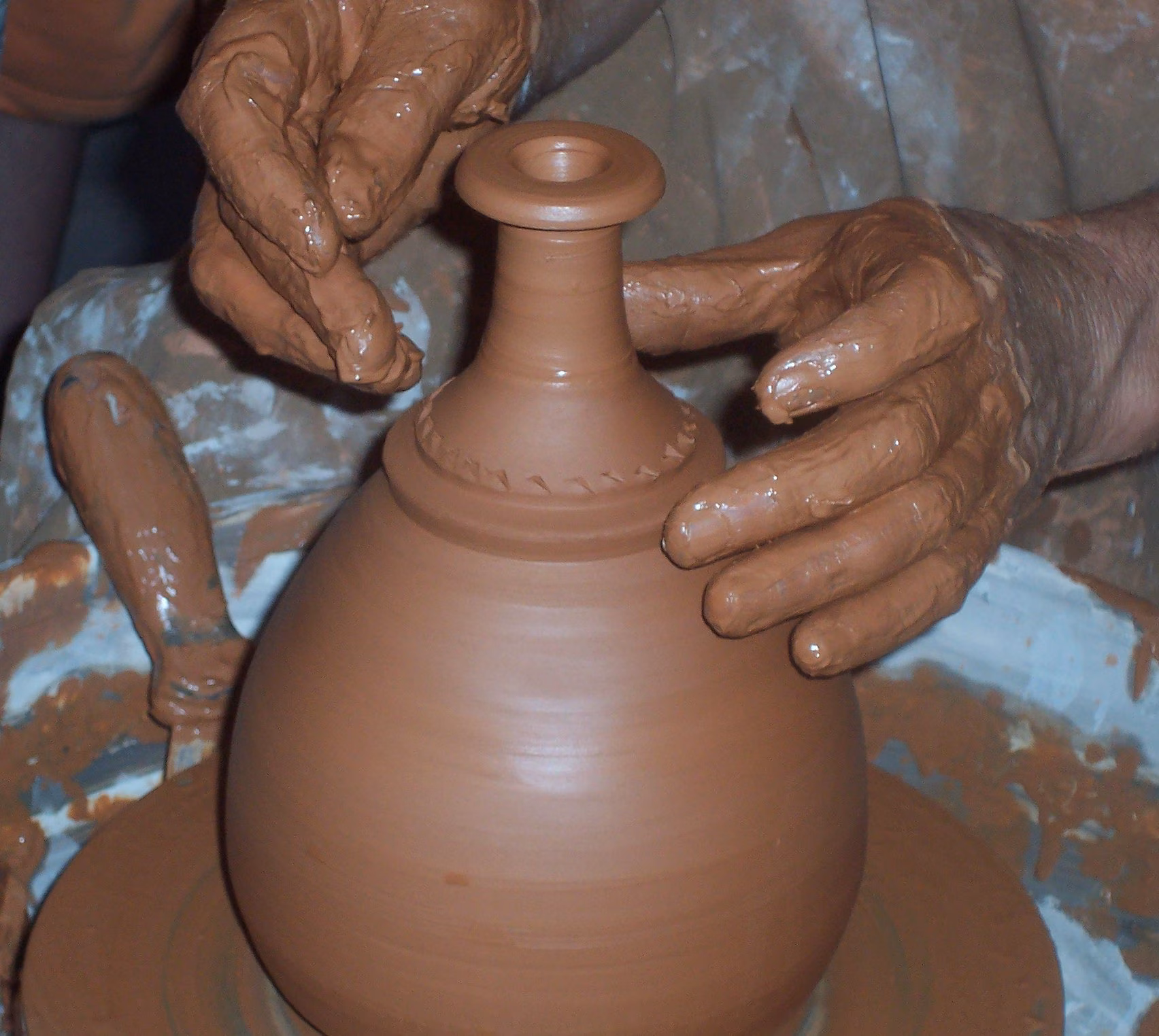 Guida Completa alle Argille da Modellare: Terracotta, Terraglia, Refrattaria, Gres e Porcellana a Confronto 4 Mani esperte di un artigiano ceramista che foggiano un vaso dal collo stretto al tornio con argilla rossa plastica fine